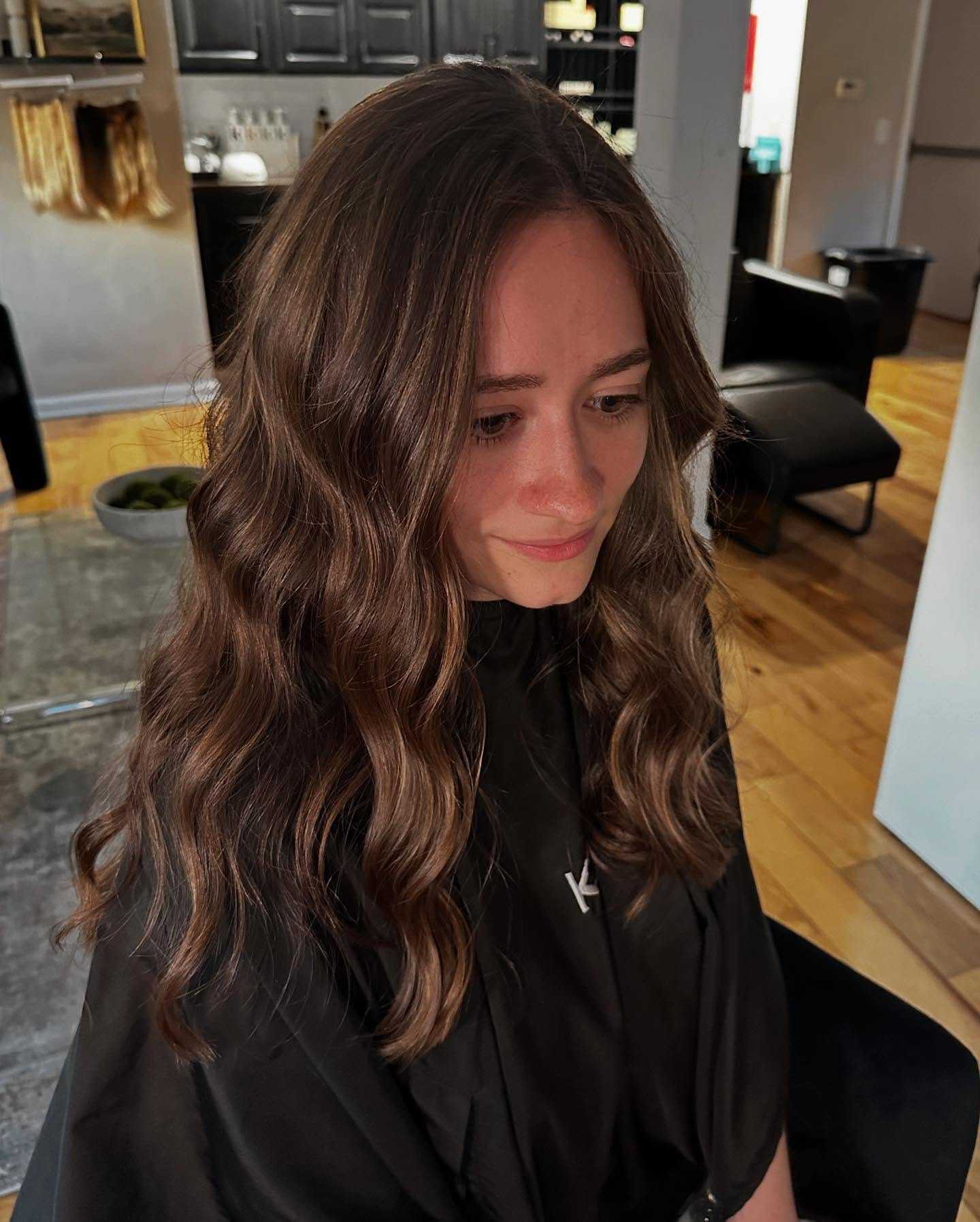 Young woman with long, wavy hair sitting in a modern salon.