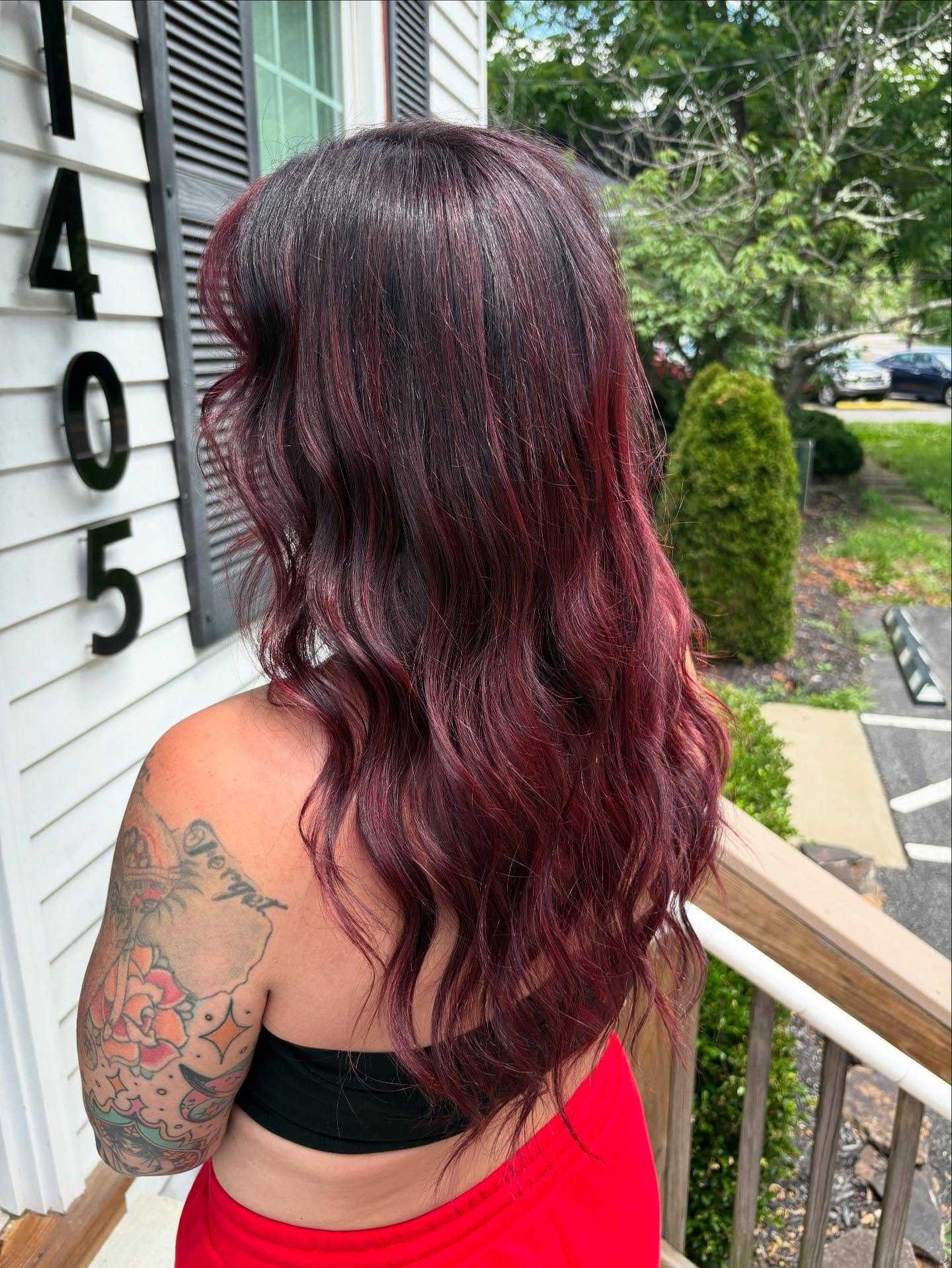 Red-haired woman with tattoos stands on porch by numbered white building.