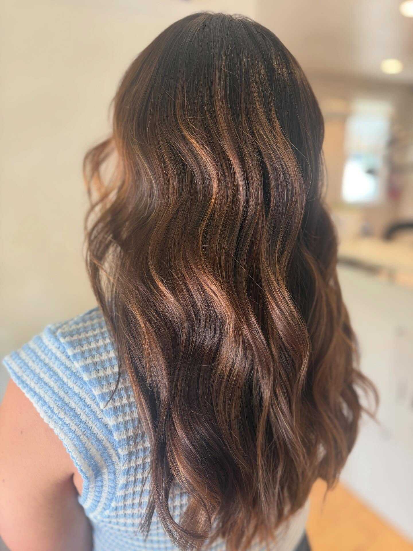 Wavy brown hair with highlights, styled in loose waves, worn by a person in a blue striped shirt.