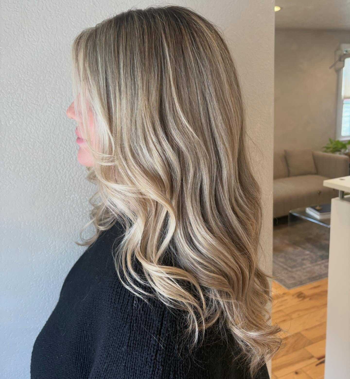 Profile of a woman with long, wavy blonde hair, wearing a black sweater indoors.